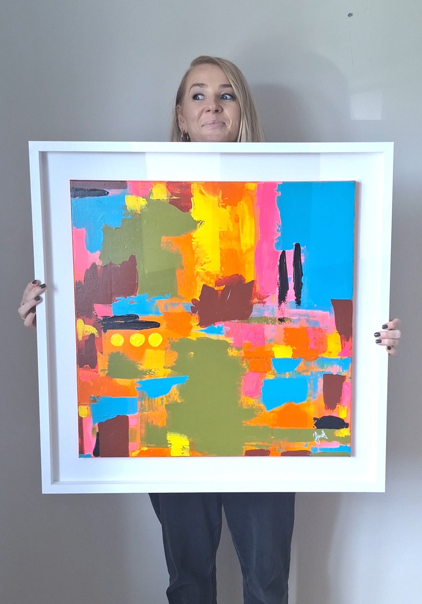 Person holding a colorful abstract painting in a white frame against a plain background
