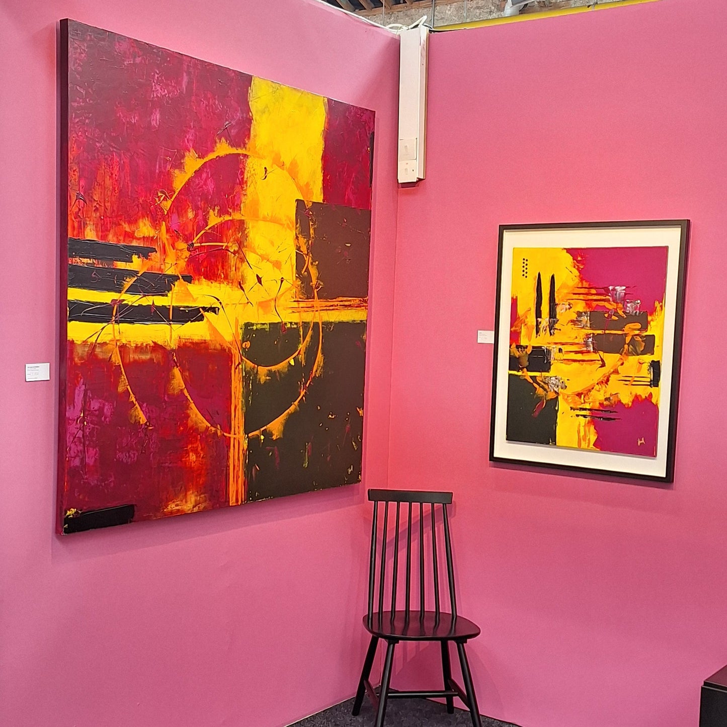 Art Fair stand set up idea with abstract paintings on pink walls and a black chair.